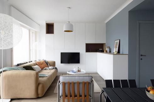 Colora – espace de vie avec façade d'armoire blanche, TV, canapé et mur bleu avec porte