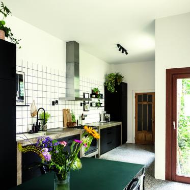 De terrazzovloer en betonnen werkblad gaat mooi samen met de zwarte keuken.